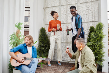 Wide angle view at diverse group of friends dancing during outdoor party at rooftop, with young man playing guitar