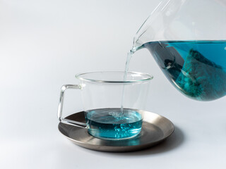 ポットからカップに青い色のハーブティーを注ぐ様子