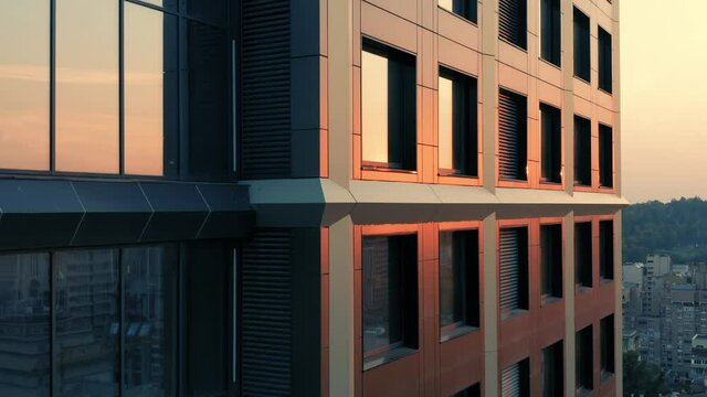 Aerial side view of a newly built apartment skyscraper with glass exterior in downtown at sunset. Close-up 