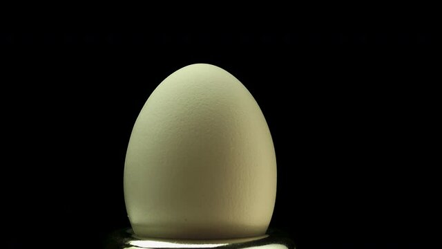 Chicken egg spinning on a black background close-up. Collect the space egg in the shell
