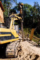 Excavator with drilling attachment boring a hole for a friction pile