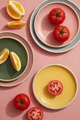 Minimal flatlay of tomato and orange on pastel plates with linen napkin. Flat lay, top view.