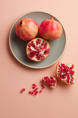 Juicy pomegranate with seeds on plate on pink pastel table top-down. copy space