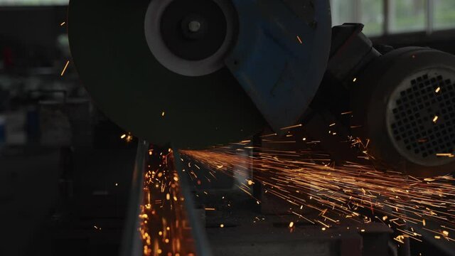 Slow motion of flywheel electric saw to cut steel in a factory Sparks splashing in the steel processing workshop Steel cutting