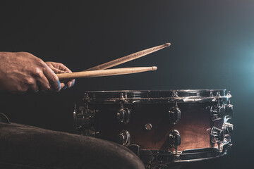 A man plays with drumsticks on a snare drum, close up.