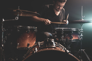 A man plays drums on stage in the dark with stage spotlights.