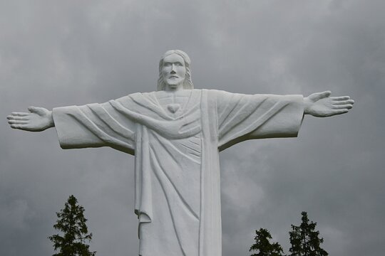 Smaller copy of Statue Of Christ The Redeemer from Rio De Janeiro, built on Grapa hill near Klin village, Namestovo district, Northern Slovakia. Cloudy summer skies, tips of coniferous trees visible.