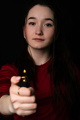 Obraz premium portrait of a girl. close-up. model in a red t-shirt, holding a fire, looking at the camera. Black background.