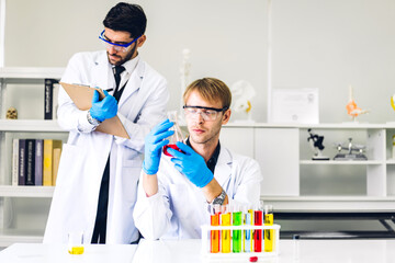 Professional two scientist man research and working doing a chemical experiment while making analyzing and mixing liquid in test tube.Young science man dropping sample chemical on glass at laboratory