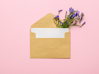 A classic postal envelope and a bouquet of flowers on a pink background. Flat lay.
