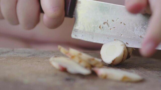 Close up hands chopping galangal, preparing ingredient for cooking thai food. Using knife sliced galangal on cutting board. Thai herb concept
