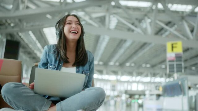 travel vacation concept,pov asian female woman wear headphone hand use laptop hand wave greeting to camera with cheerful and happiness,asian female sit wating at wating area in airport terminal