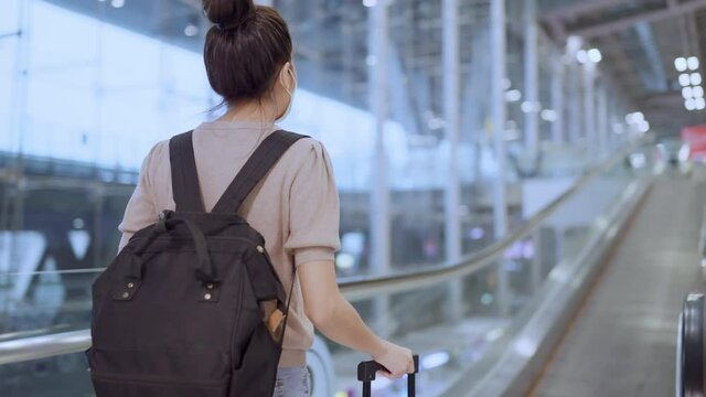 Back view of asian female woman traveling with backpack and suitcase on escalator in airport terminal,travel lifestyle after covid lockdown is over asian female traveller on the way to abroad