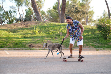 Young tattooed man walking his dog and riding a longboard.
