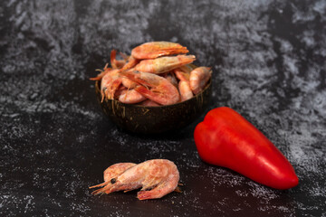 red paprika and quick-frozen prawns in an eco-friendly coconut bowl on a dark background