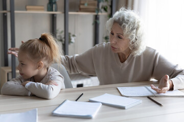 Fototapeta na wymiar Worrying older mature grandmother talking to upset small granddaughter, stuck with hard task, feeling stressed while studying at home or preparing for exams, learning problems, education concept.
