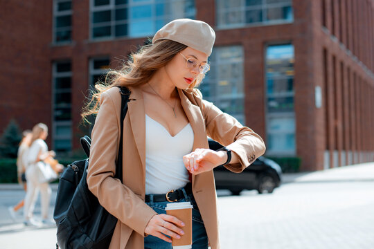 Young confident stylish millenial girl standing in city center and checking time on her hand watch