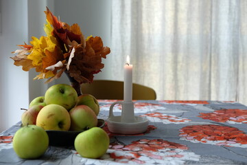 White candle on the table with green apples and orange autumn leafes. 