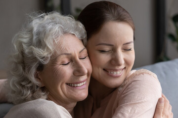 Close up head shot devoted happy middle aged mature mother embracing attractive grownup daughter, feeling thankful or showing sweet tender candid emotions, sincere diverse family relations concept.