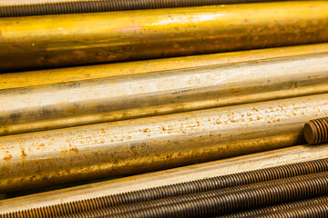 Large bronze round bars and steel threaded rods lie on a shelf, close-up.
