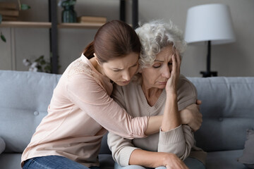Worried stressed young woman cuddling depressed emotional unhappy middle aged old retired mother,...