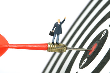 Fototapeta premium Miniature people toy figure photography. A businessman standing above red arrow going to the center of dartboard while raise his hand. Isolated on white background.