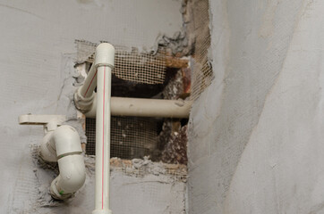 Gray plastic pipes against the plastered wall. Piping with corner fittings and flap. Inside the room. Construction industry. Plumbing services. Selective focus.