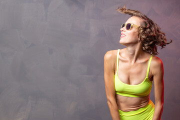Portrait of young model posing against of grey background in sunglasses and yellow swimsuit	