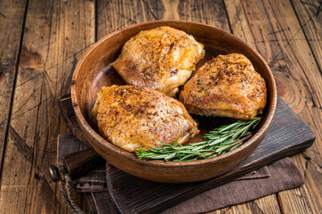 Roasted chicken thighs in a wooden plate with rosemary and herbs. wooden background. Top View