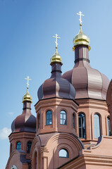Fototapeta na wymiar A Christian Orthodox church opposite a clear blue sky. A red brick building with golden domes. Religion, faith.