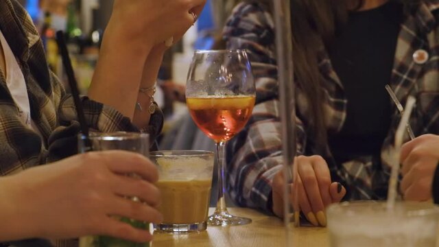 a group of girls in plaid shirts are sitting in a cafe, they have glasses on the table with different alcoholic cocktails that they drink, aperol spritz, baileys frappe, mojito
