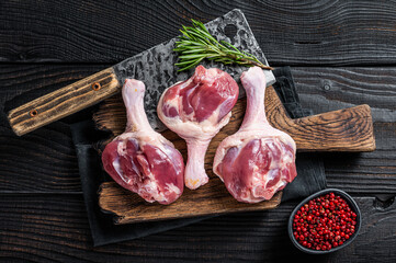 Raw Duck thighs on butcher board with meat cleaver. Black wooden background. Top view