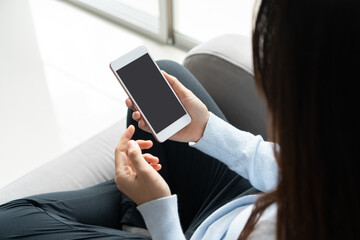 Woman hands using mobile phone while sitting on sofa in living room at home. Business, technology and lifestyle concept. Copy space