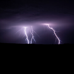 Fototapeta na wymiar Multiple lightning strikes painting the sky purple on a summer evening during a thunderstorm