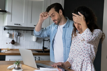 Millennial spouses standing in kitchen at home calculate household expenditures, manage family...