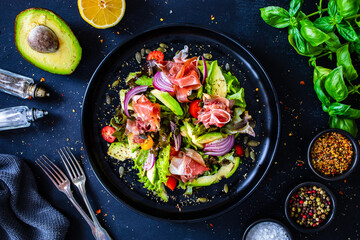 Tasty salad - ham, avocado, mini tomatoes and fresh green vegetables on wooden background
