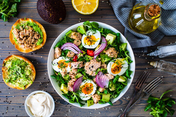 Tuna salad - tuna, avocado, hard boiled eggs, cherry tomatoes, lettuce and onion on wooden table
