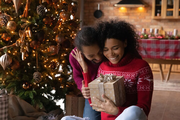 Fototapeta na wymiar Loving happy young African American couple sit near fir tree exchange gifts on New Year at home. Smiling millennial biracial man and woman celebrate Christmas Eve together. Winter holiday concept.