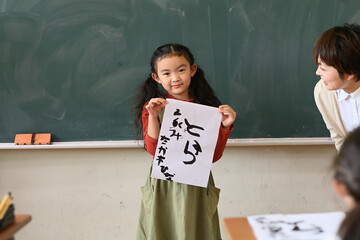 2022年の干支「寅年」の文字を習字で書いた、小学生の女の子が学校の教室で発表するシーン。習字に書いている名前は仮名なので、本名ではありません。 - obrazy, fototapety, plakaty