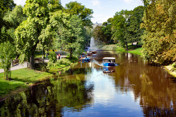 Fototapeta na wymiar LATVIA, RIGA, AUGUST, 2021 - Pleasure boats cruise along the Riga river canal in Riga central city park, capital of Latvia