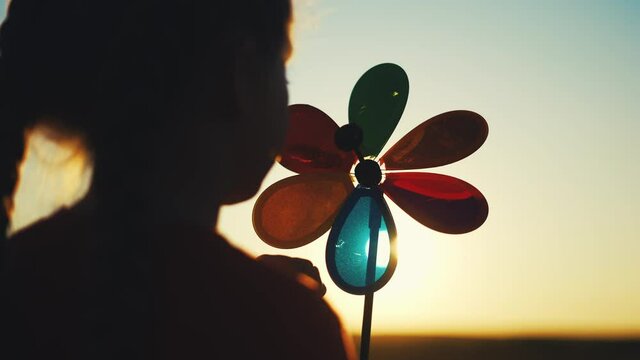 kid pinwheel. little baby girl silhouette play with windmill toy wind in the park. happy family kid dream concept. baby girl play toy pinwheel the glare of the sun at sunset in the park fun