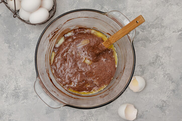 Chocolate pastry for making a sponge cake with melted butter in a bowl on a gray concrete...