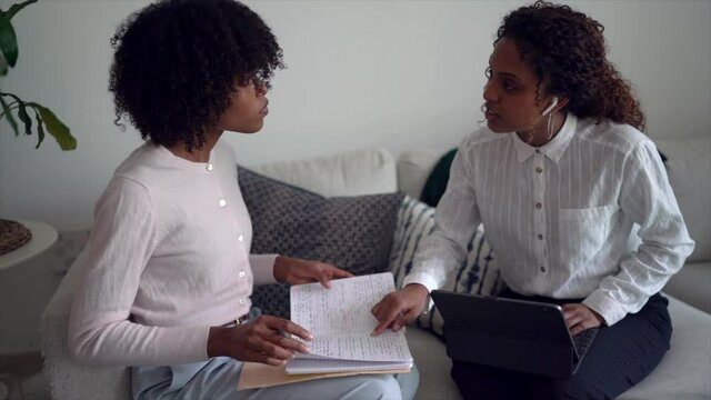 Two young business professional black women having interview conversation wearing smart casual sitting on sofa using tablet