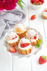 Delicious homemade small cakes profiterole choux pastry with custard, strawberry and icing powder on the white wooden background. Copy space.