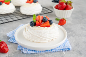 Pavlova meringue cake with whipped cream and fresh berries on top on a plate on a gray concrete background. Summer dessert. Copy space.