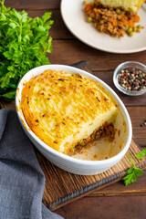 Homemade Shepherd's Pie in the casserole dish on a dark wooden background. Traditional British dish with minced meat and mashed potatoes.