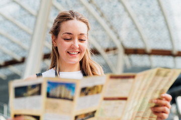 Young caucasian woman traveller holding tourist map smiling discovering and sightseeing