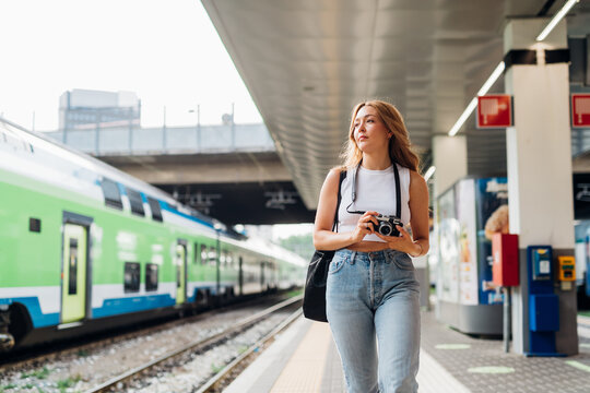 Young caucasian woman tourist walking platform railway station taking photograph
