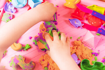 Obraz na płótnie Canvas Hands of a child playing with multicolored kinetic sand