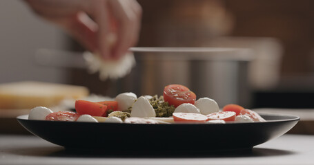 man sprinkle penne with mozzarella, tomatoes and pesto with aged grated cheese